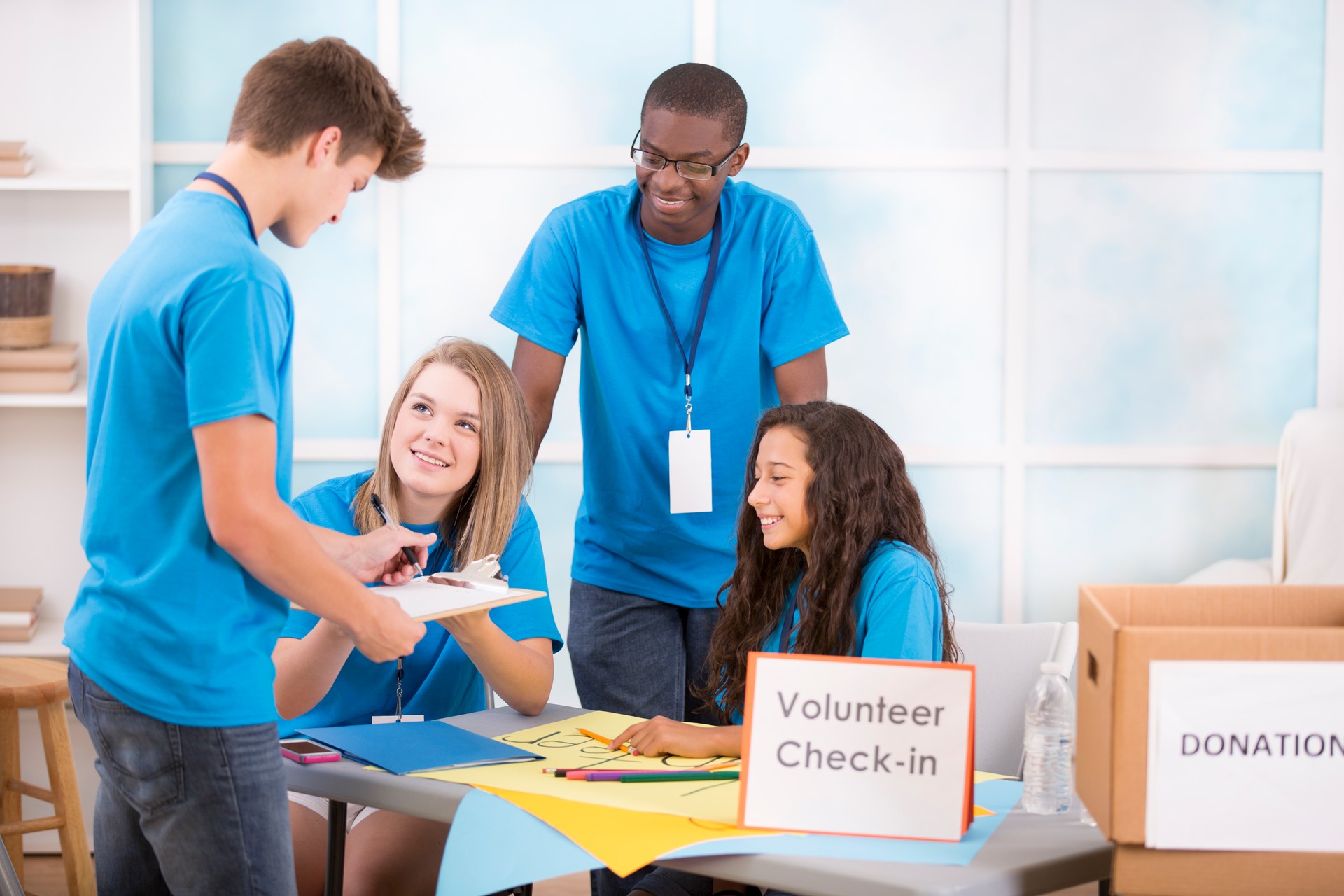 Teen boy registers at volunteer check-in table. Multi-ethnic group.